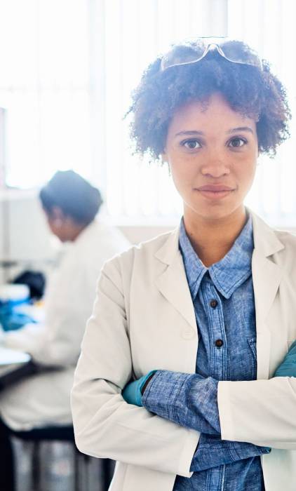 Young scientist standing in a lab with colleagues working in the background